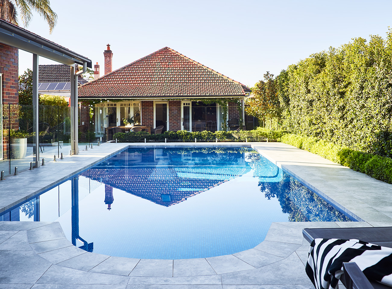 Gallery Image Modern family pool with tiled surround, glass fence and classic home backdrop