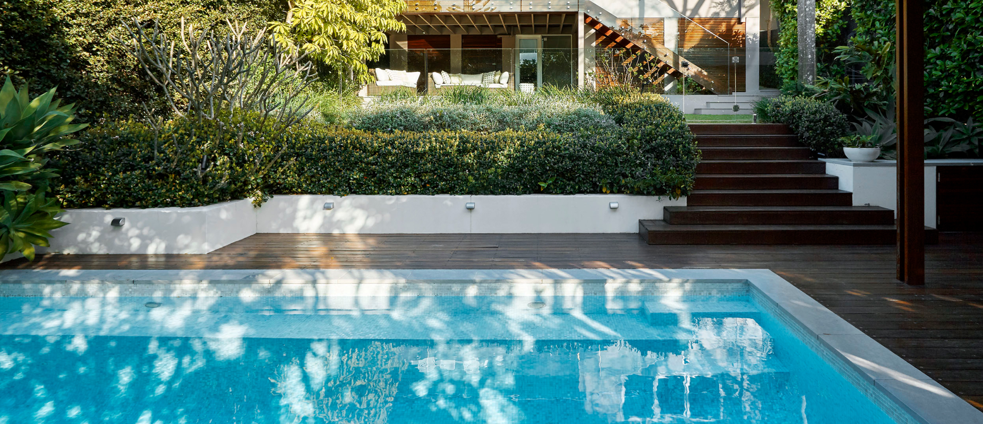 Custom pool design in Sydney featuring a modern rectangular swimming pool, timber decking, landscaped gardens and luxury outdoor entertaining area.