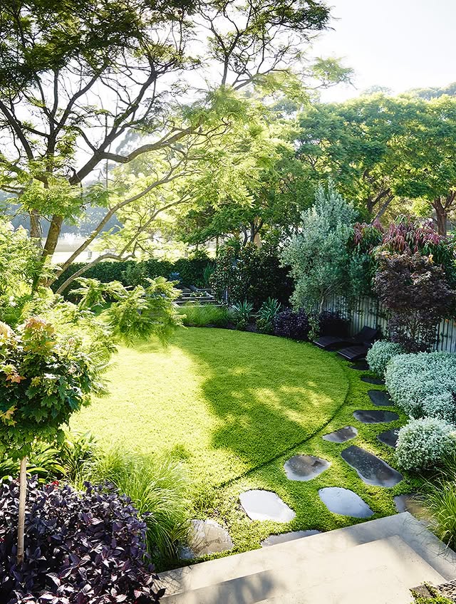 Landscaped garden with lush lawn, mature trees, layered planting and natural stone stepping pavers.
